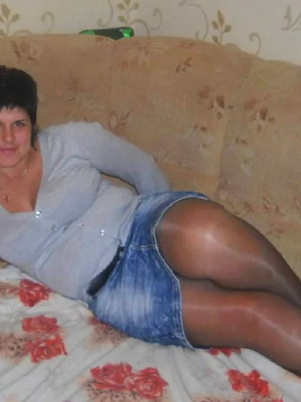 Personne allongée sur un canapé, vêtue d'une veste claire, d'une jupe en jean et de collants foncés, devant un fond floral.
