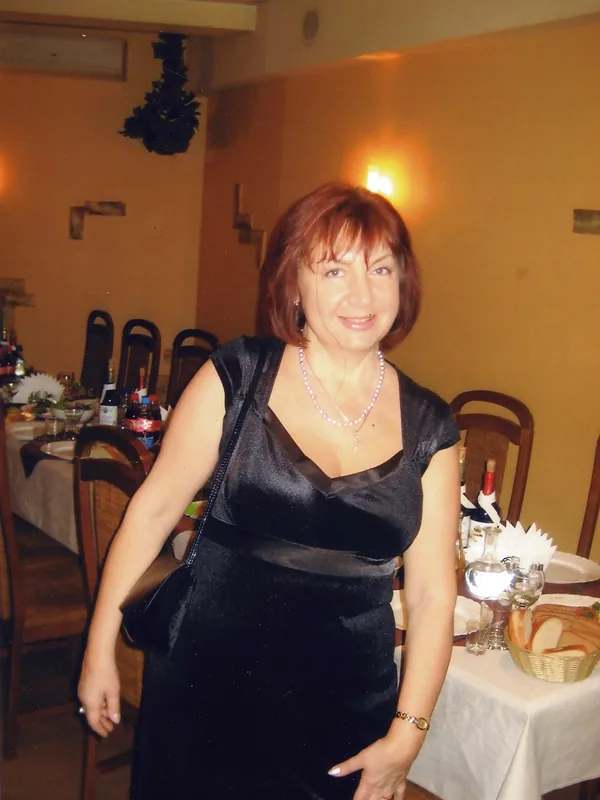 Portrait d'une personne en robe noire, souriante, dans un restaurant, avec collier de perles et sac à bandoulière