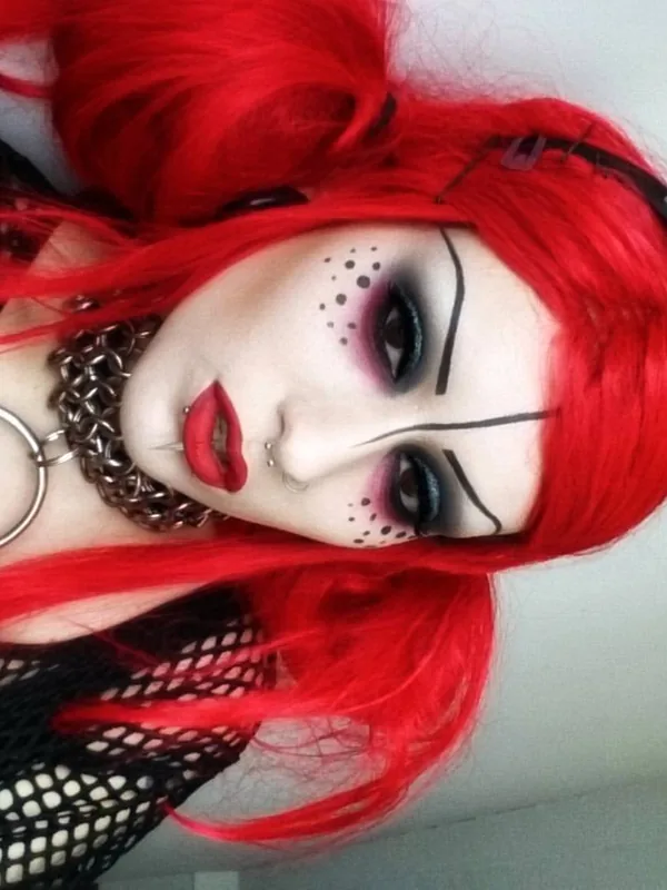 Portrait d'une personne aux cheveux rouges, maquillage gothique, piercings, collier en chaîne, maille noire, couronne à pointes